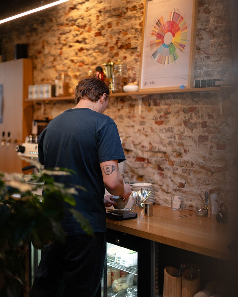 A barista working the counter against an exposed brick wall hung with a flavor wheel poster
